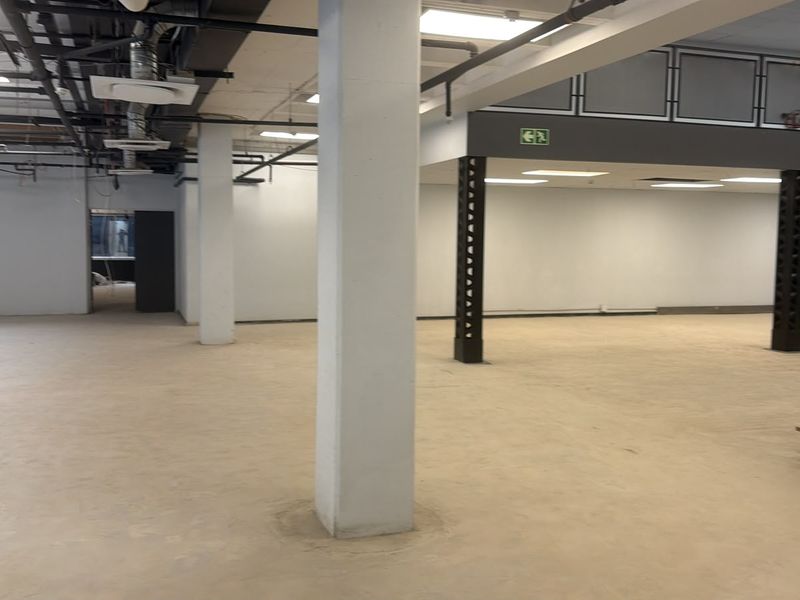 Spacious open-plan commercial interior featuring industrial exposed ceilings, structural columns, a mezzanine level, and a metal staircase with concrete flooring.
