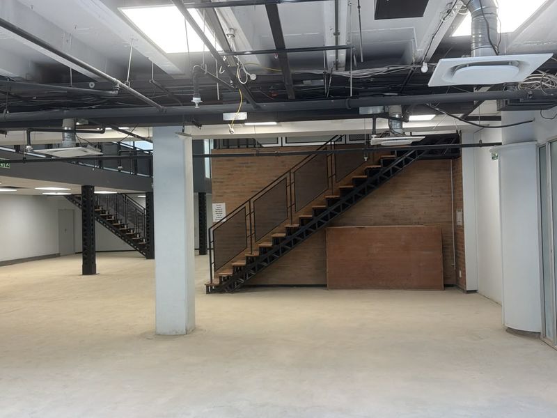 Spacious open-plan commercial area featuring an industrial aesthetic with exposed ceilings, brick accents, and a central steel staircase.