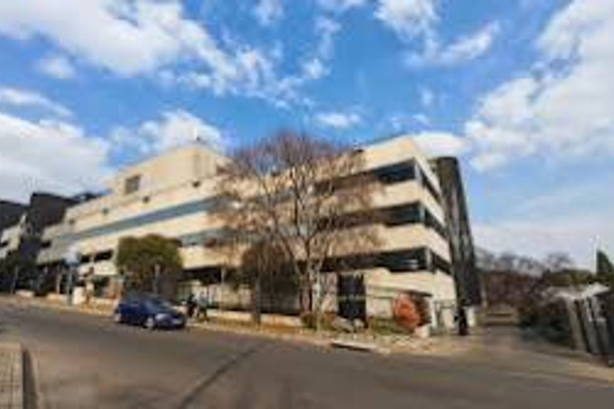 A street-level view of a multi-story commercial building featuring a paved driveway and perimeter fencing along the road frontage.