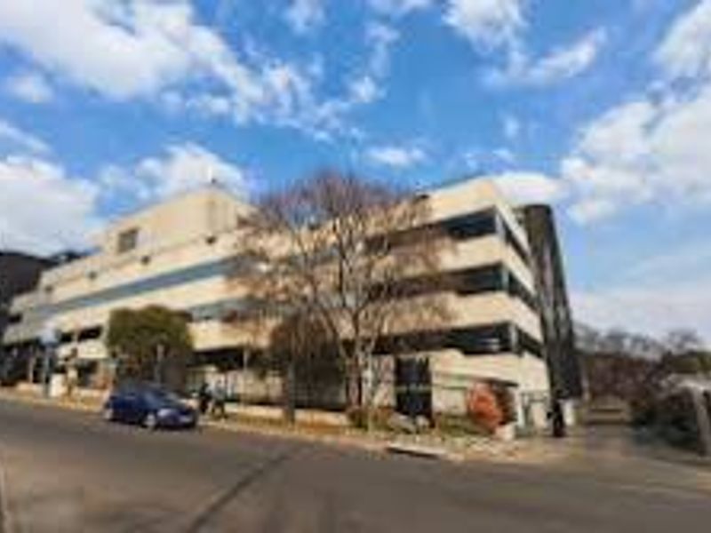 A street-level view of a multi-story commercial building featuring a paved driveway and perimeter fencing along the road frontage.