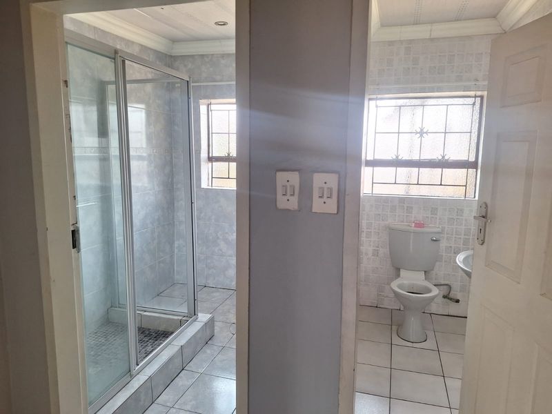 A functional bathroom featuring a separate shower enclosure, toilet, and wash basin with tiled finishes and security bars on the windows.