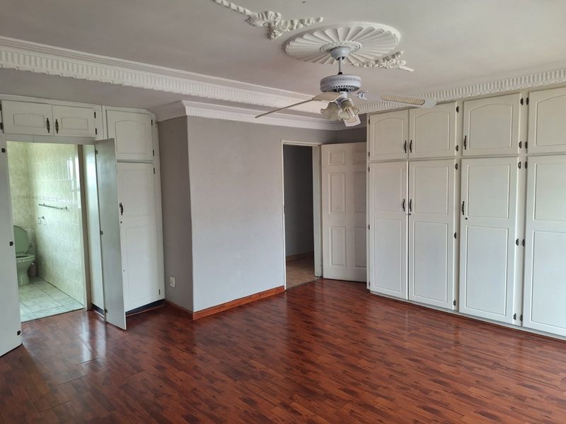 Spacious bedroom featuring extensive built-in cabinetry, ceiling fan with decorative rose, and laminate flooring, with an adjoining en-suite bathroom.