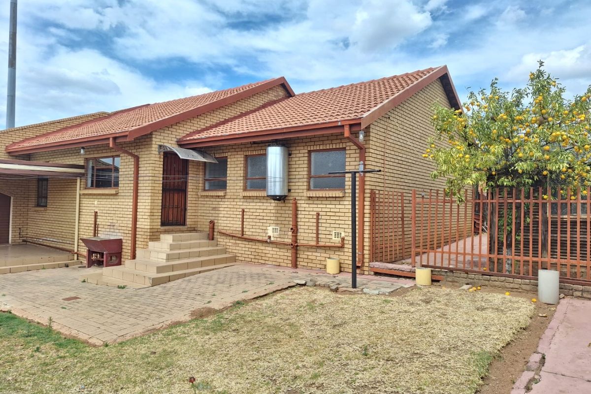 Rear view of a face brick house featuring a paved patio area, external geyser, and secure metal fencing.