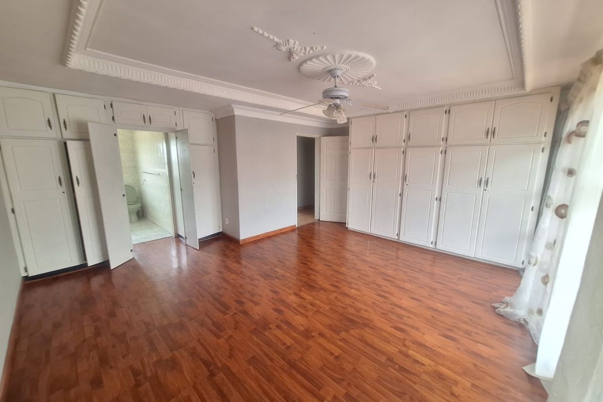 Spacious bedroom featuring extensive built-in cabinetry, decorative ceiling detailing, a ceiling fan, and laminate flooring, with direct access to an en-suite bathroom.
