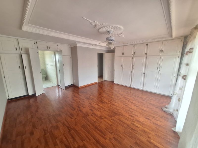 Spacious bedroom featuring extensive built-in cabinetry, decorative ceiling detailing, a ceiling fan, and laminate flooring, with direct access to an en-suite bathroom.