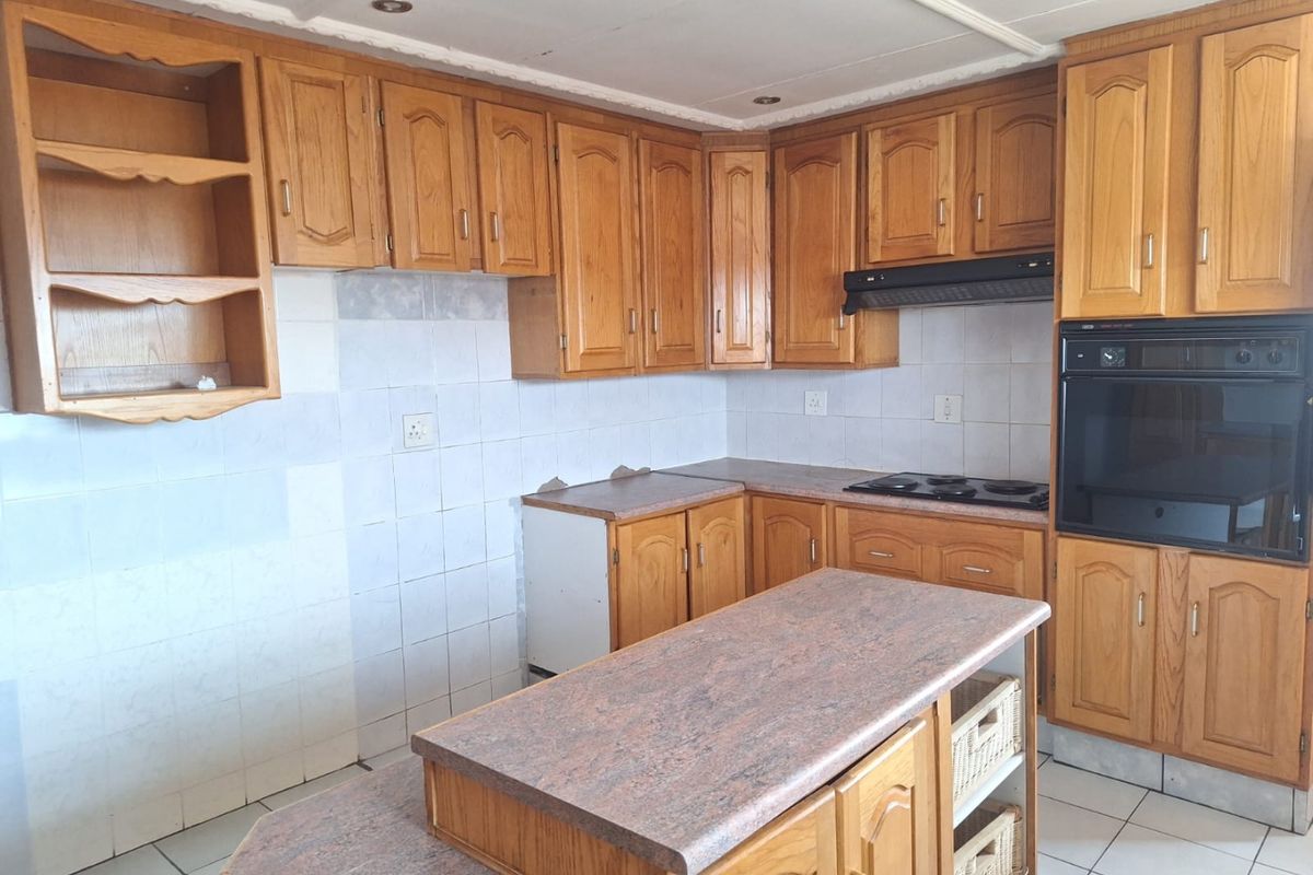 A dated kitchen featuring wooden cabinetry, a built-in oven, hob, extractor fan, and a central island with stone-look countertops.