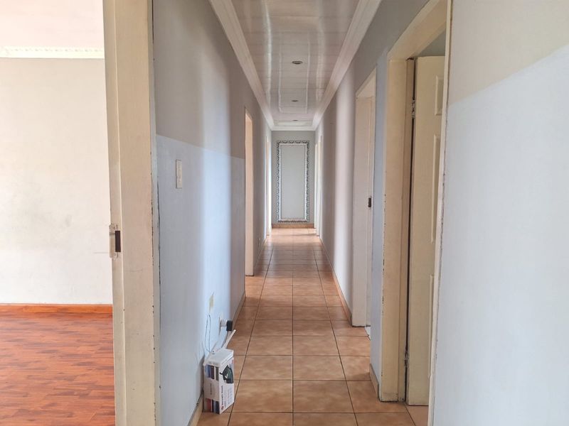 A long, empty hallway featuring tiled flooring, recessed ceiling lighting, and multiple internal door access points.