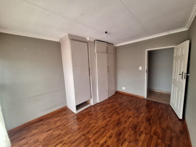 An empty bedroom featuring laminate flooring, built-in cupboards, and decorative ceiling cornicing, presenting a blank canvas for potential updates.