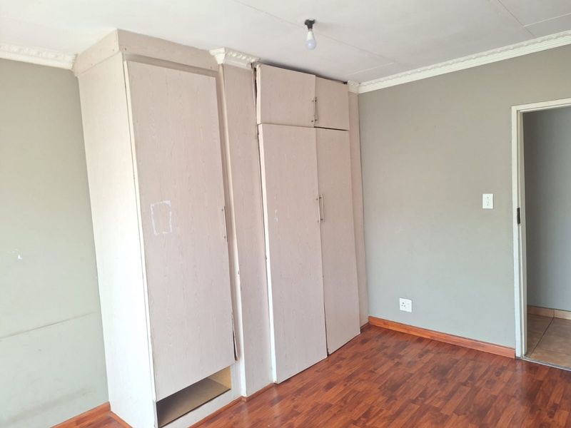 A bedroom featuring laminate flooring and built-in cupboards with visible wear and misalignment, requiring minor repairs or cosmetic updates.