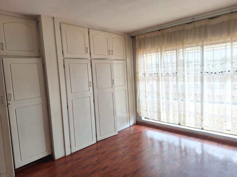 A bright, empty bedroom featuring extensive built-in cabinetry, laminate flooring, and large windows with security bars.