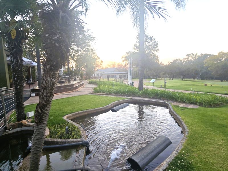 A landscaped garden area featuring a decorative water feature, paved pathways, and a wooden deck overlooking the surrounding estate grounds.