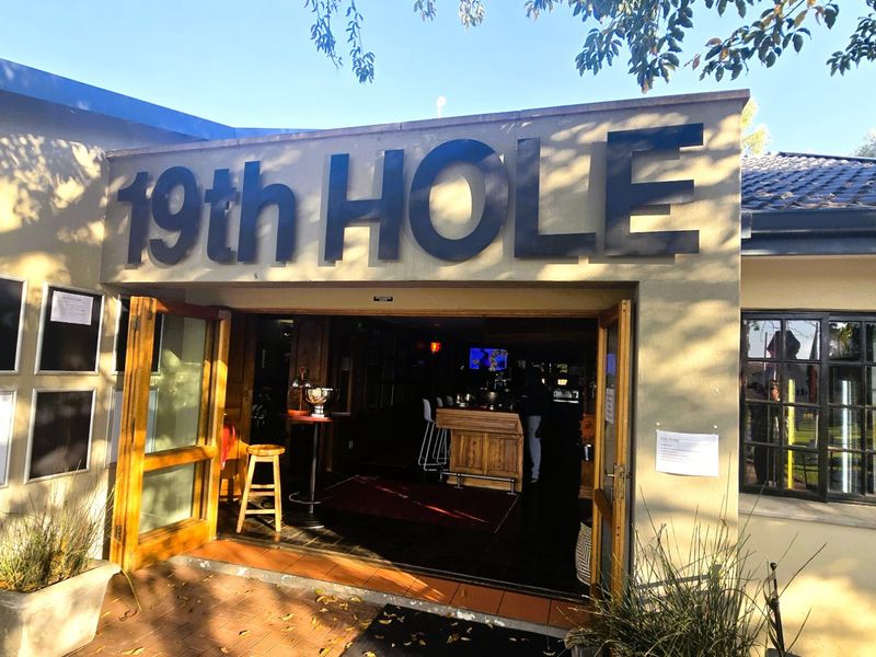 Entrance to the 19th Hole clubhouse featuring timber-framed glass doors and prominent exterior signage.
