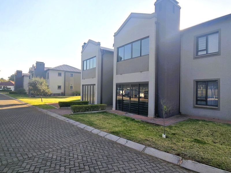 A modern double-storey residential townhouse featuring a paved driveway, landscaped garden, and large aluminium-framed windows and sliding doors.