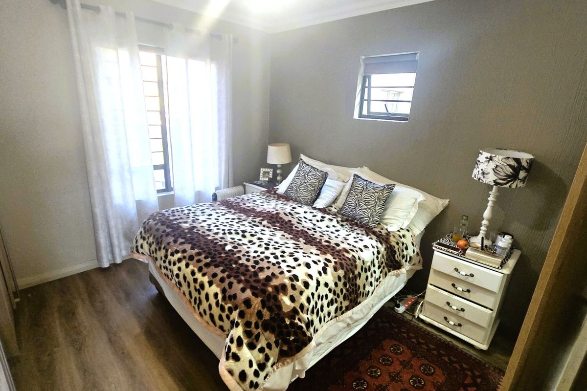 A cozy bedroom featuring laminate flooring, built-in cupboards, and security bars on the windows, providing a functional and private sleeping space.