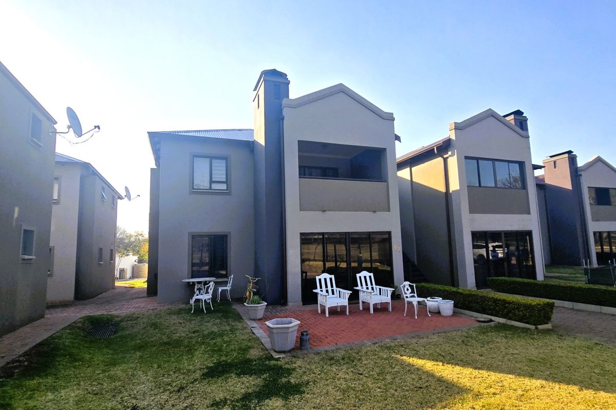 Rear view of a multi-story residential unit featuring a brick-paved patio, sliding glass doors, and a private balcony overlooking a landscaped garden area.