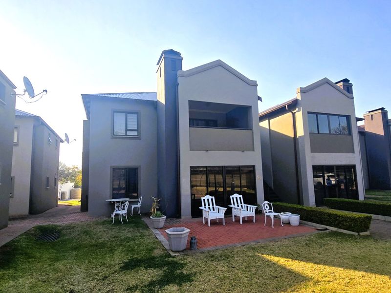 Rear view of a multi-story residential unit featuring a brick-paved patio, sliding glass doors, and a private balcony overlooking a landscaped garden area.