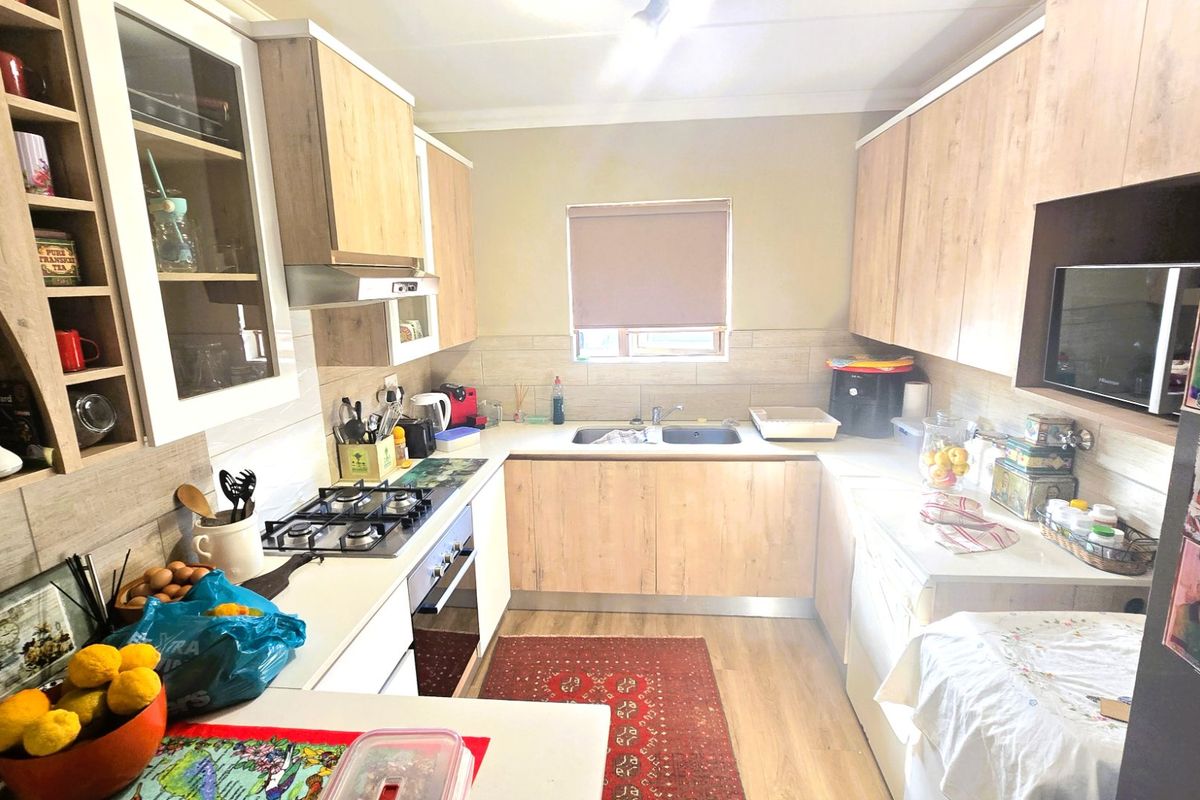A functional kitchen featuring light wood-look cabinetry, a gas hob with extractor, under-counter oven, and a double basin sink with tiled backsplash.