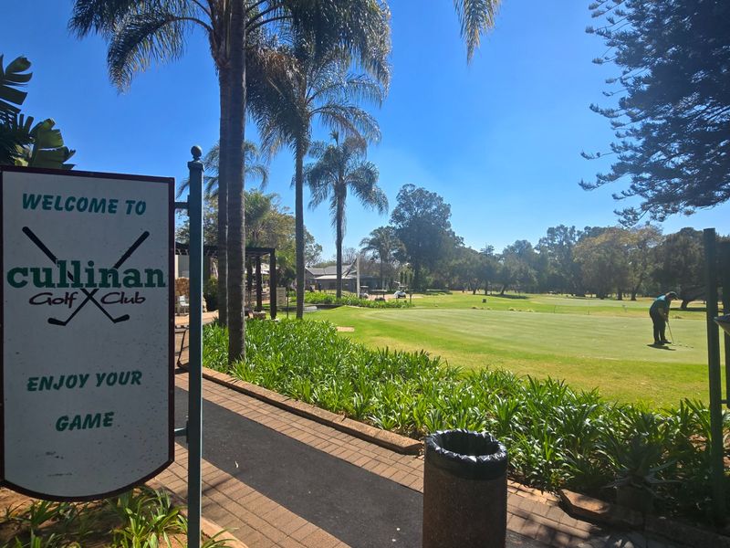 A scenic view of the Cullinan Golf Club grounds featuring a paved walkway, manicured lawns, and mature palm trees.