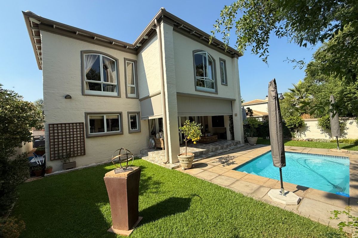 Rear view of a two-story house featuring a swimming pool, stone patio area, and well-maintained garden space.