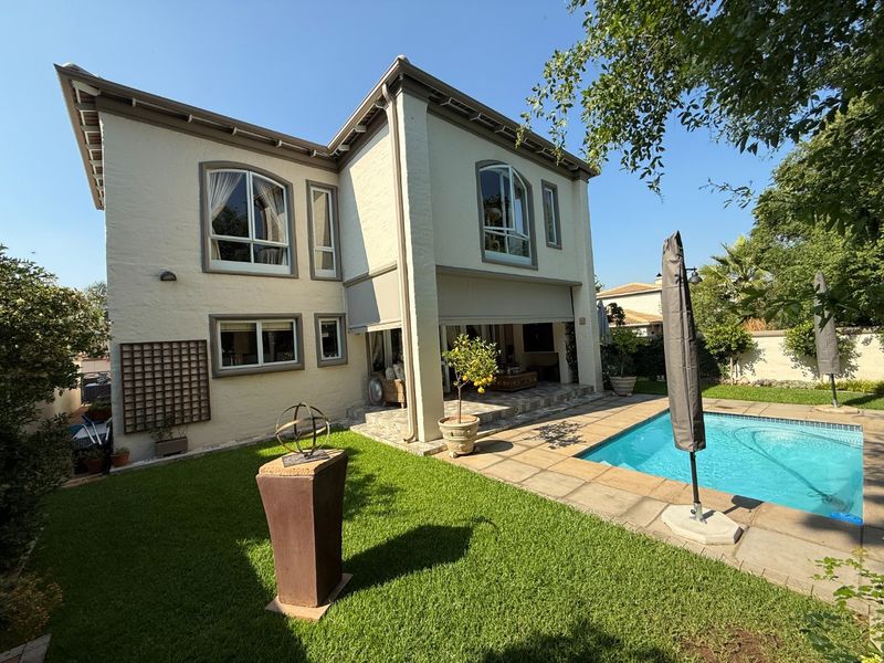 Rear view of a two-story house featuring a swimming pool, stone patio area, and well-maintained garden space.