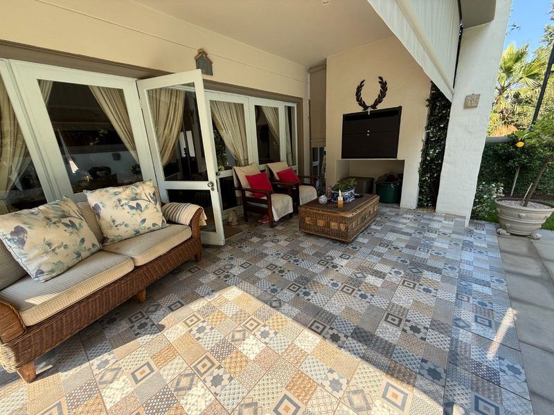 A covered patio area featuring decorative patterned floor tiles and a built-in braai, providing seamless access to the interior through large french doors.