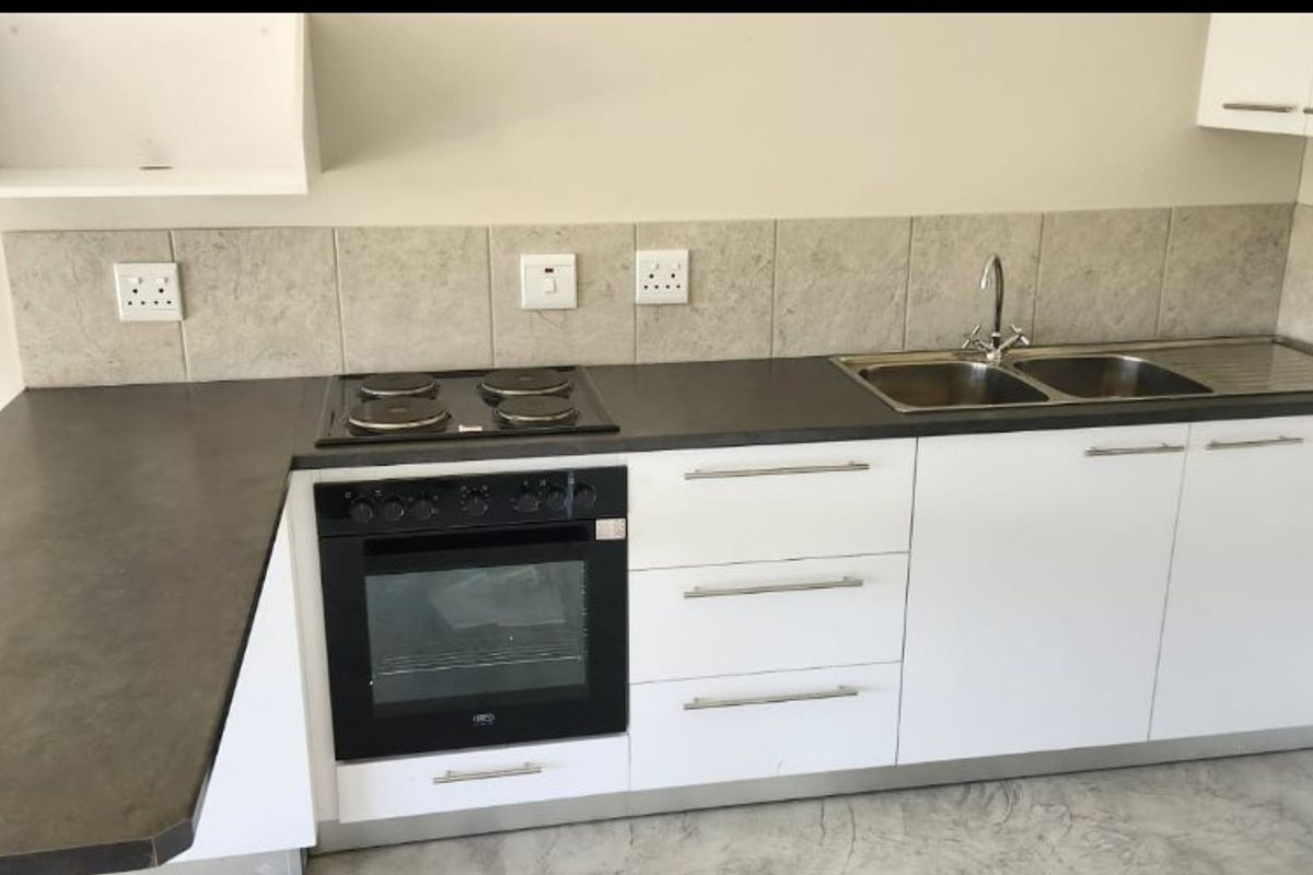 A clean, modern kitchen featuring white cabinetry, dark laminate countertops, a built-in oven, electric hob, and a stainless steel double sink.
