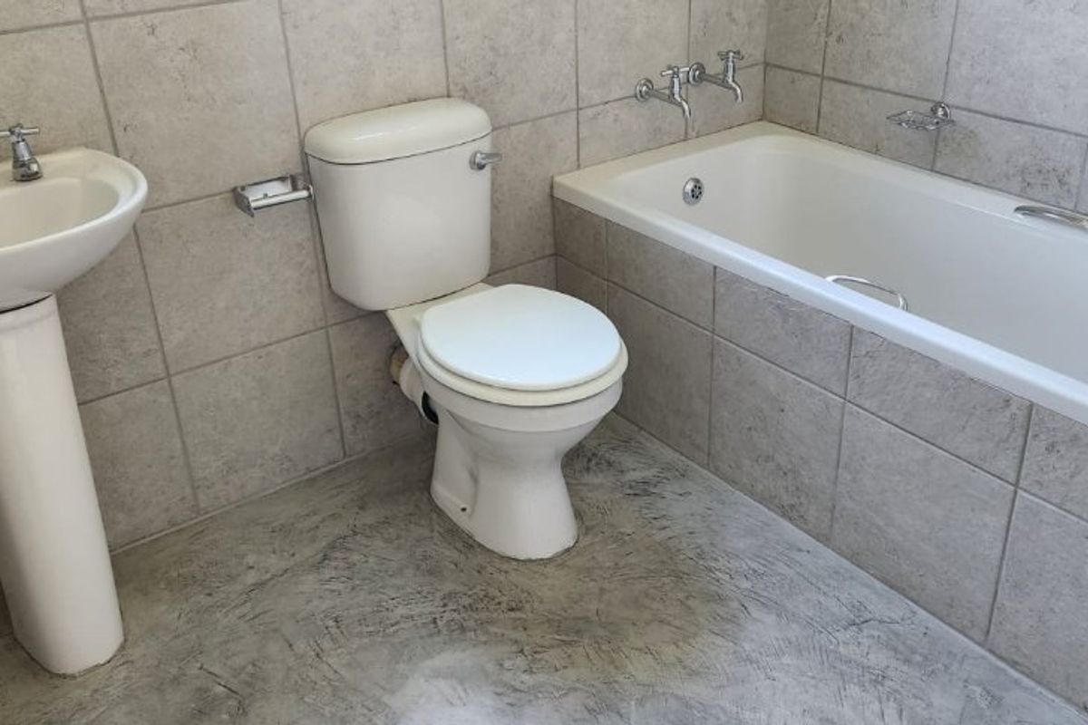 A functional bathroom featuring a pedestal basin, standard toilet, and a built-in bathtub with tiled walls and flooring.