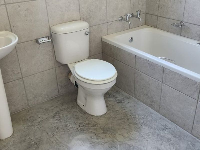 A functional bathroom featuring a pedestal basin, standard toilet, and a built-in bathtub with tiled walls and flooring.