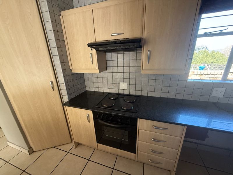 A functional kitchen featuring light wood cabinetry, black granite countertops, a built-in oven, electric hob, and tiled finishes throughout.