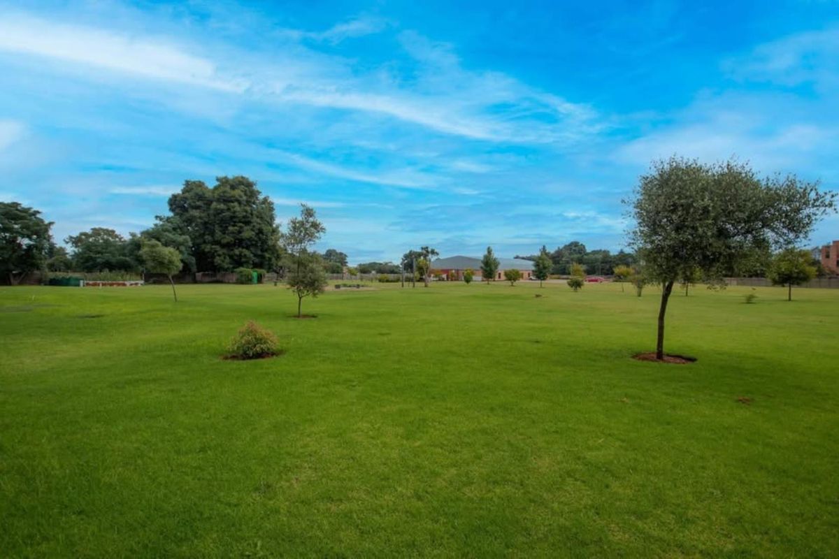 A spacious, well-maintained residential plot featuring expansive green lawns and established trees, offering a clear and open landscape.