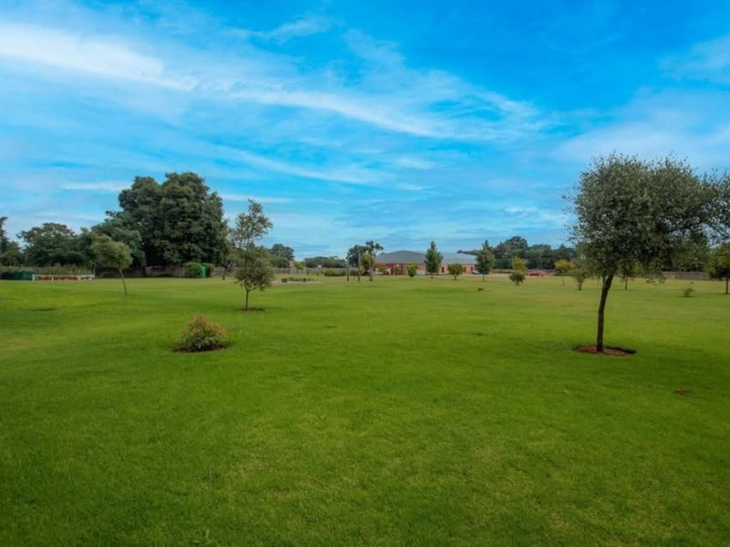 A spacious, well-maintained residential plot featuring expansive green lawns and established trees, offering a clear and open landscape.