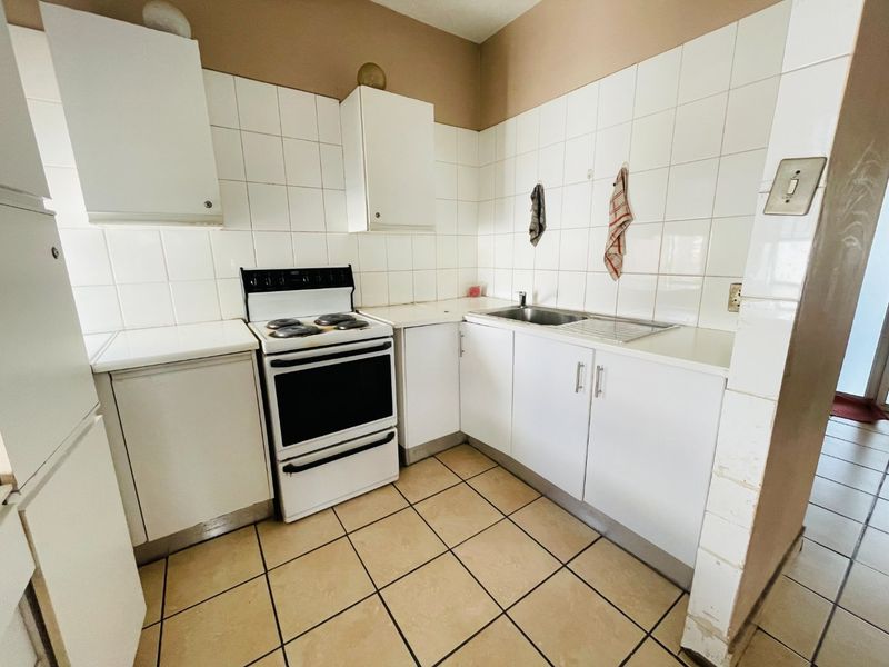 Compact kitchen featuring white cabinetry, tiled backsplash, a freestanding stove, and a stainless steel sink with tiled flooring.