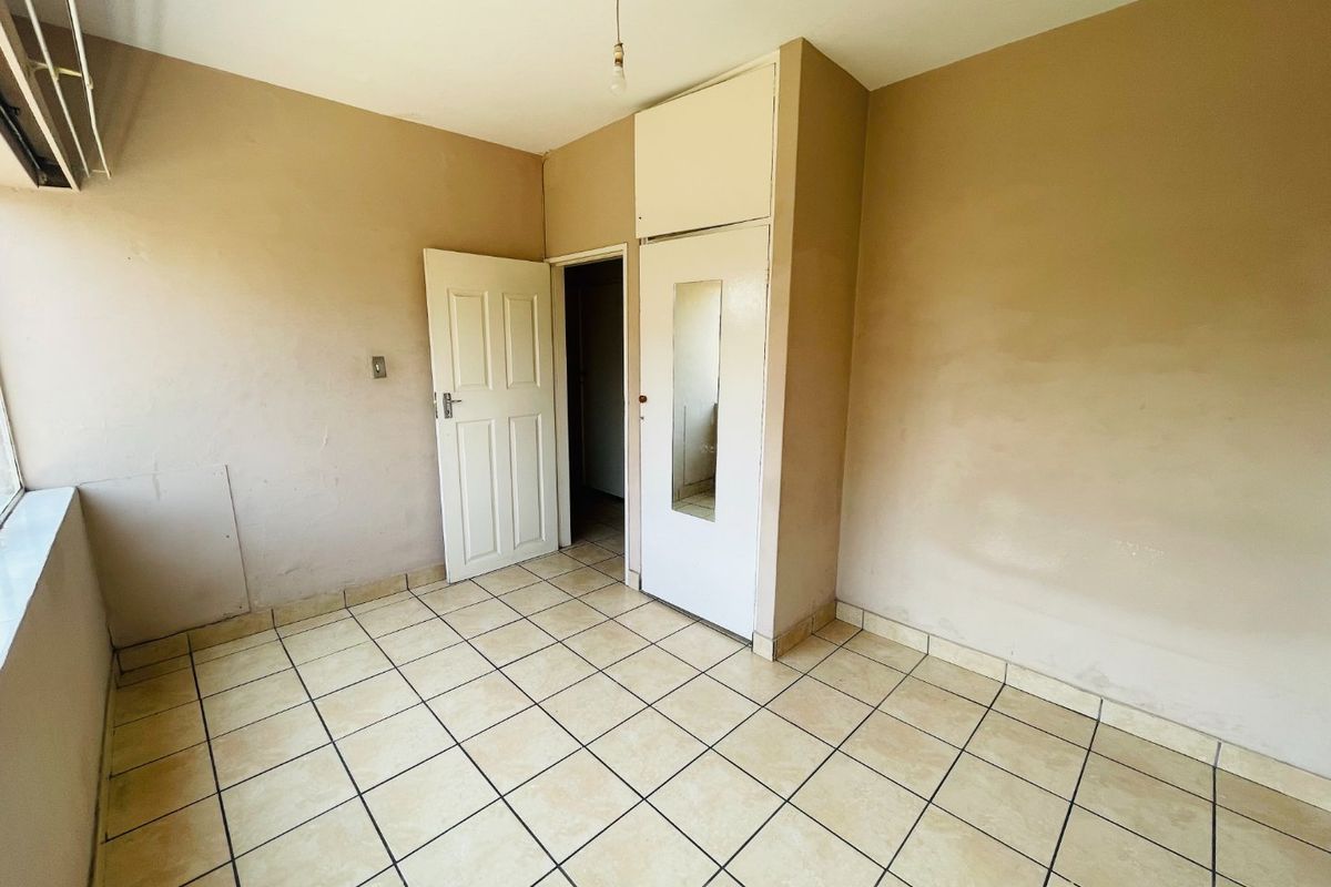 An empty bedroom featuring tiled flooring, a built-in wardrobe with a mirror, and neutral wall finishes, ready for personalization.