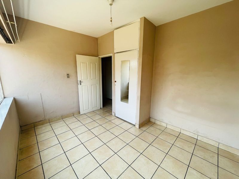 An empty bedroom featuring tiled flooring, a built-in wardrobe with a mirror, and neutral wall finishes, ready for personalization.