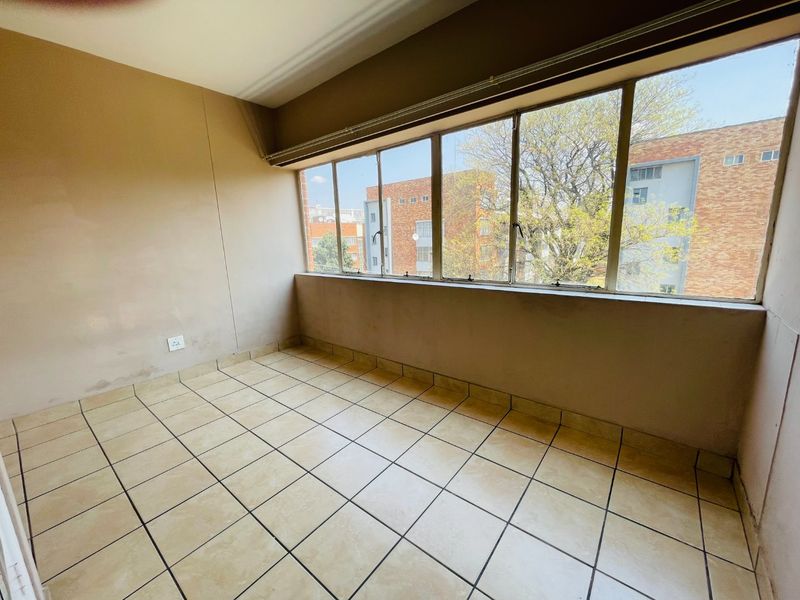 An empty, enclosed balcony featuring tiled flooring and a large window bank with views of the surrounding apartment complex.