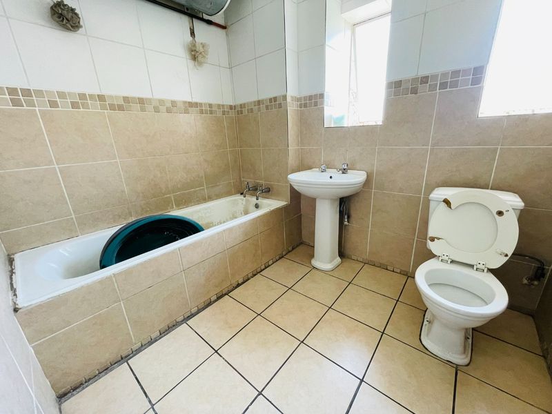 A dated bathroom featuring a bathtub, pedestal basin, and toilet with neutral wall and floor tiling.