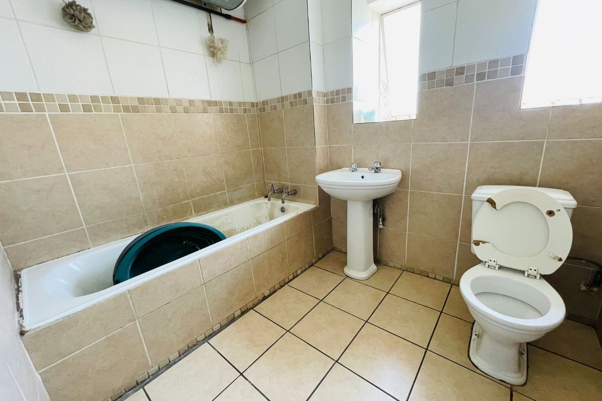 A dated bathroom featuring a pedestal basin, bathtub, and toilet with neutral wall and floor tiling, requiring cosmetic updates and fixture maintenance.