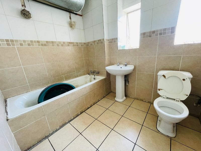 A dated bathroom featuring a pedestal basin, bathtub, and toilet with neutral wall and floor tiling, requiring cosmetic updates and fixture maintenance.