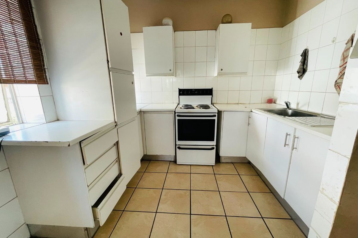 A dated kitchen featuring white cabinetry, tiled splashbacks, a freestanding oven, and tiled flooring, offering potential for a modern renovation.