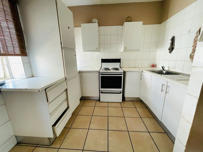 A dated kitchen featuring white cabinetry, tiled splashbacks, a freestanding oven, and tiled flooring, offering potential for a modern renovation.