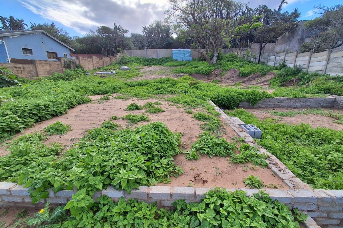 A vacant residential plot featuring a perimeter wall and partial brick foundation, currently overgrown with vegetation.