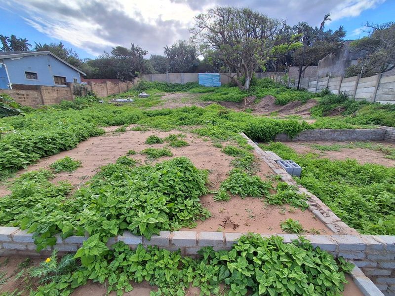 A vacant residential plot featuring a perimeter wall and partial brick foundation, currently overgrown with vegetation.