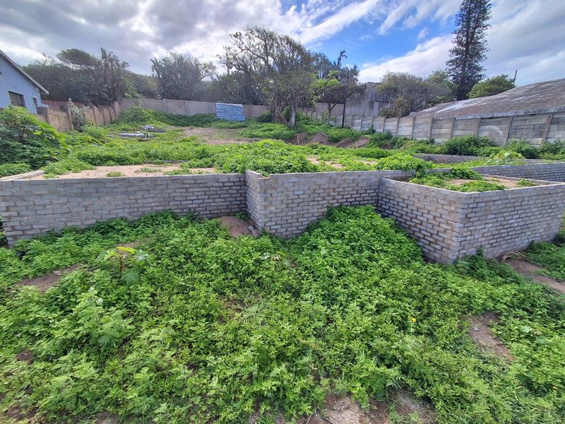 Vacant residential land featuring partial brick foundation walls and perimeter boundary fencing, currently overgrown with vegetation.