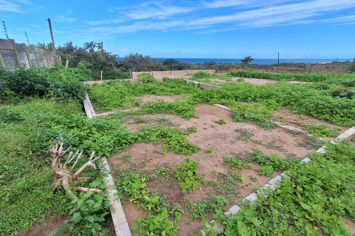 Vacant residential land featuring a concrete foundation slab, perimeter boundary walls with electric fencing, and ocean views in the distance.