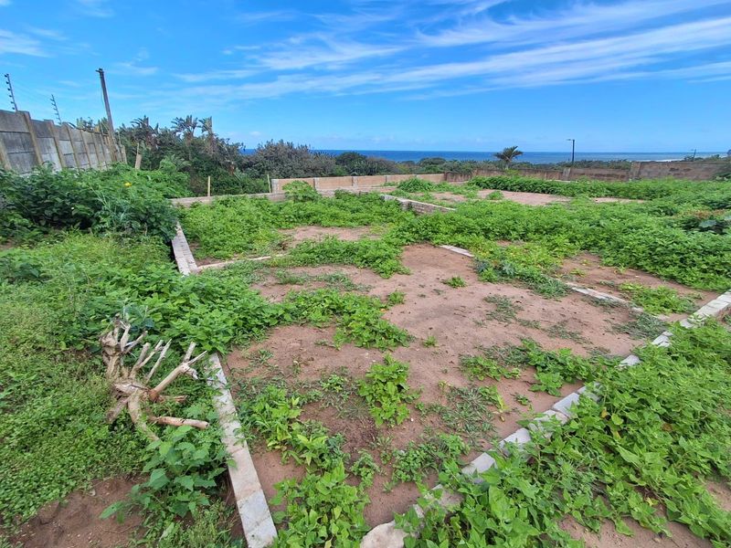 Vacant residential land featuring a concrete foundation slab, perimeter boundary walls with electric fencing, and ocean views in the distance.