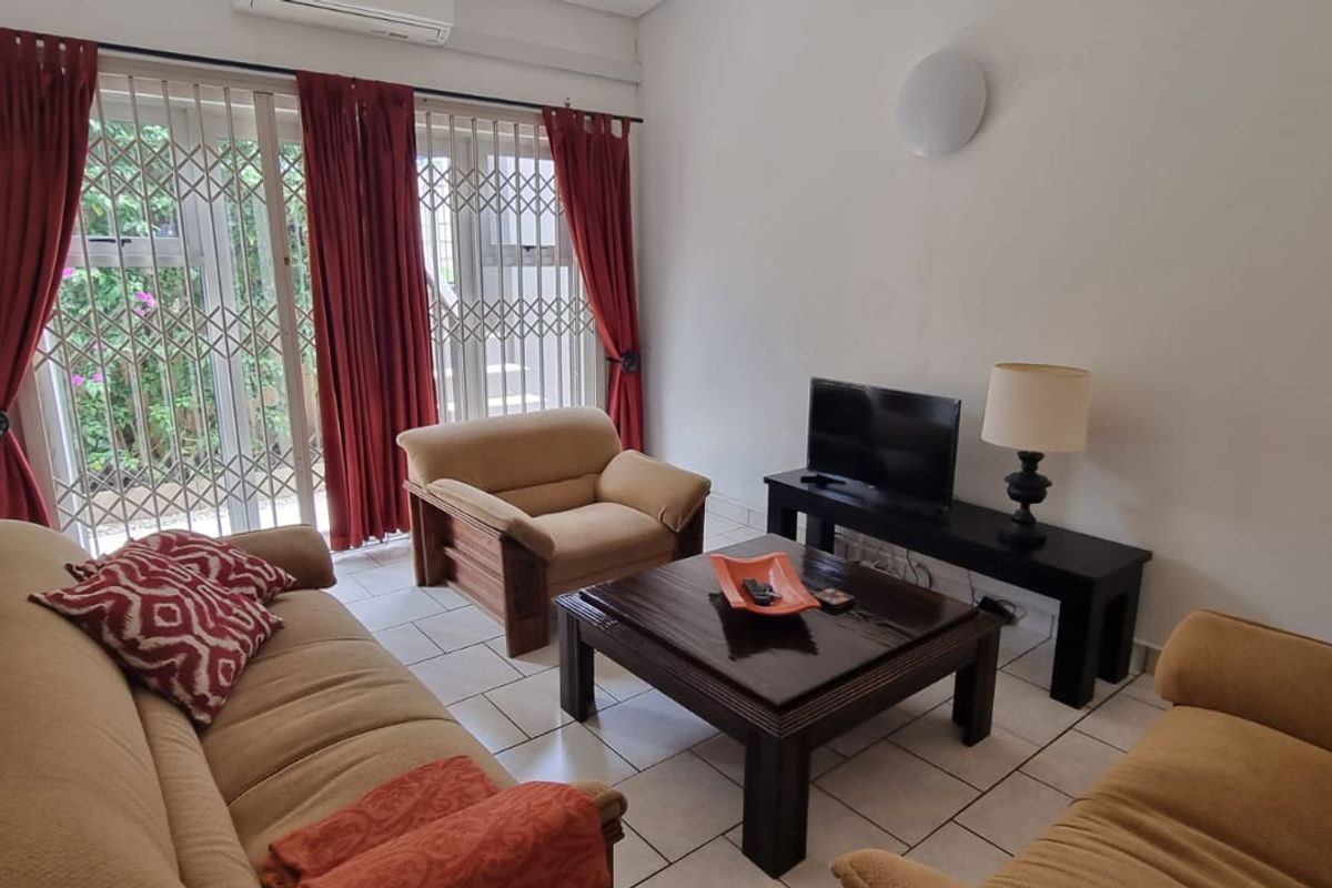 A living room featuring tiled flooring, a wall-mounted air conditioning unit, and a sliding glass door with an integrated security gate.
