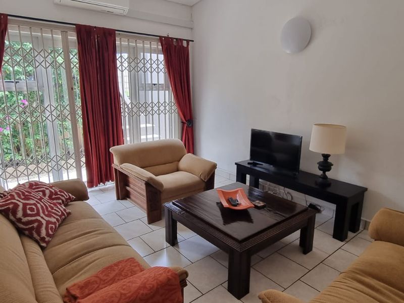 A living room featuring tiled flooring, a wall-mounted air conditioning unit, and a sliding glass door with an integrated security gate.