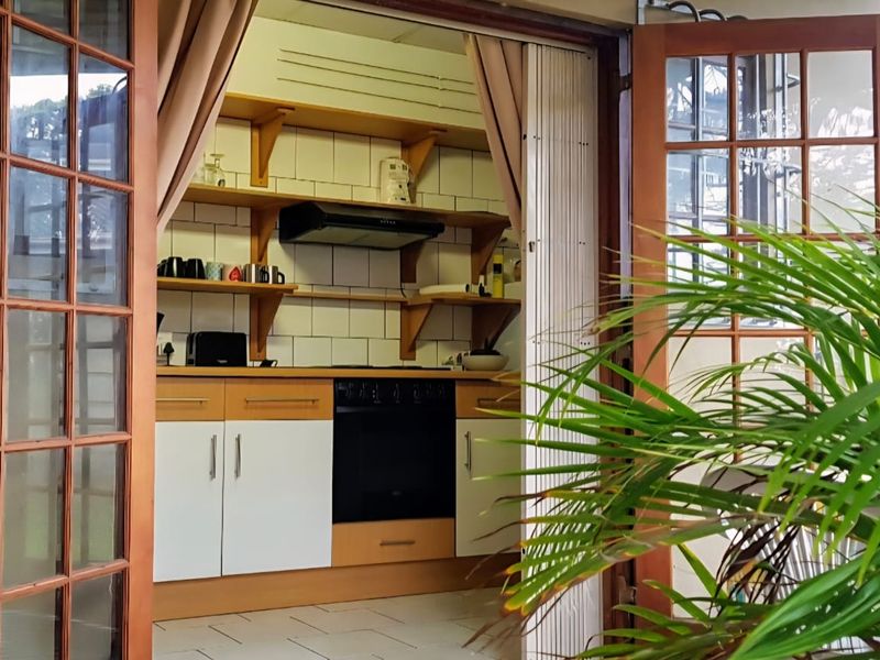 Compact kitchen featuring built-in oven, extractor fan, tiled backsplash, and open wooden shelving, accessible via wooden french doors.