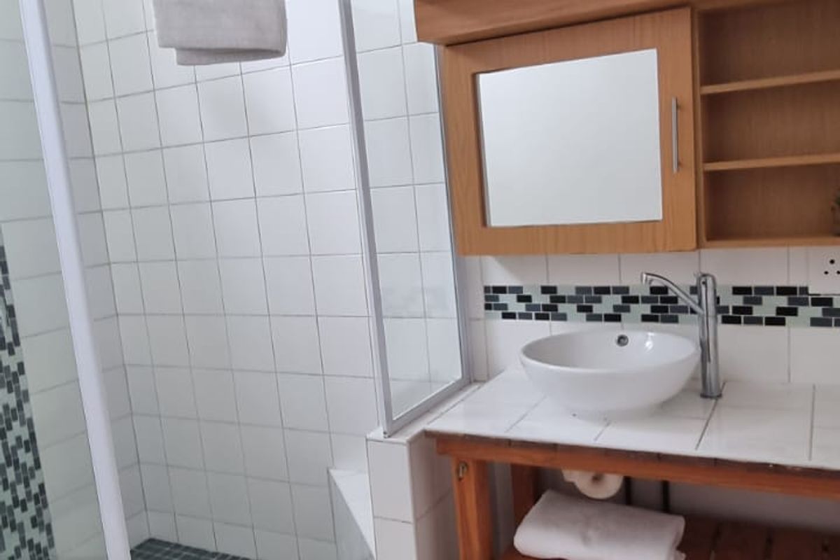 A functional bathroom featuring a corner shower enclosure, a vessel sink vanity with integrated storage, and neutral floor tiling.
