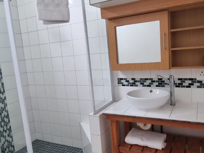 A functional bathroom featuring a corner shower enclosure, a vessel sink vanity with integrated storage, and neutral floor tiling.